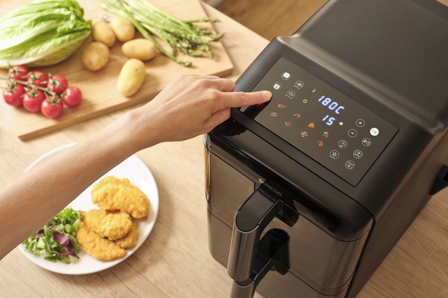 Fritéza teplovzdušná Sencor SFR 1250BK čierna Detail dotykového ovládacieho panelu teplovzdušnej fritézy Sencor SFR 1250BK, kde používateľ nastavuje teplotu a program prípravy. Na kuchynskej linke sú pripravené čerstvé suroviny ako paradajky, špargľa a zemiaky, zatiaľ čo vedľa stojí tanier s hotovými chrumkavými kúskami.