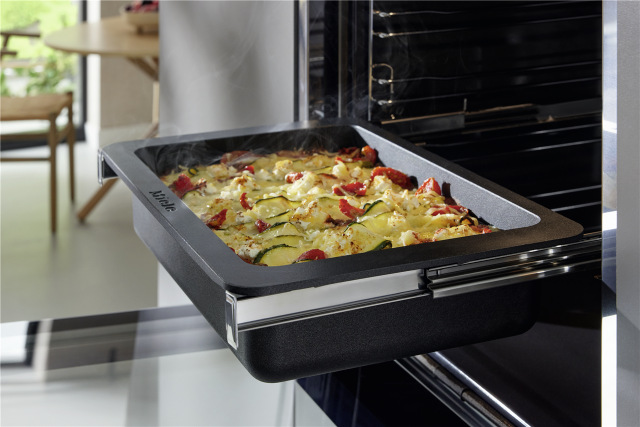 Rúra Miele DGC 7250 CulinArt Nerezová ocel/čistá ocel nerez Otvorená parná rúra Miele DGC 7250 vstavaná v kuchyni s pečenou zeleninou na plechu.