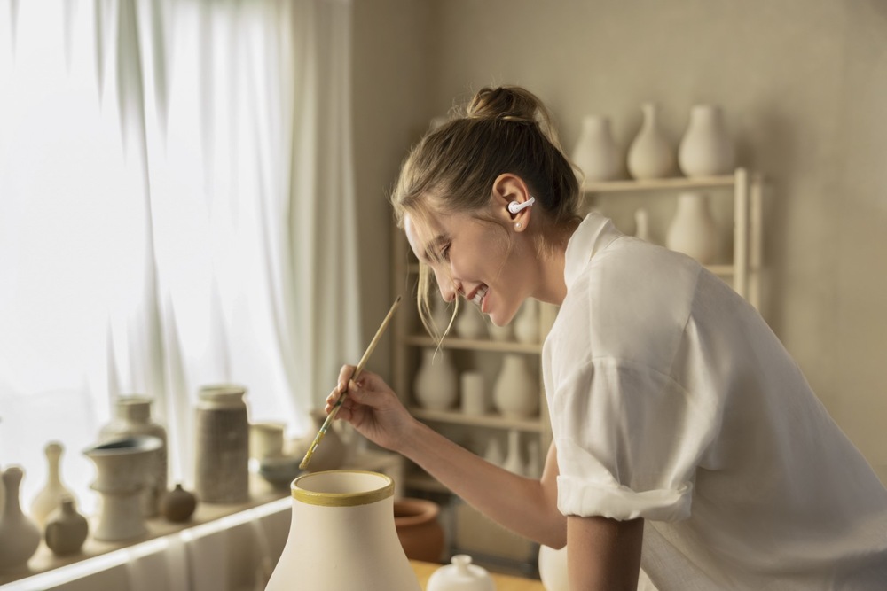 Slúchadlá Shokz OpenDots 2, Bluetooth biela Žena s otvorenými slúchadlami maľujúca keramickú vázu