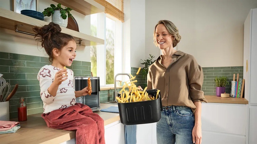 Fritéza teplovzdušná Bosch Serie 6 MAF671C0 béžová Dcéra sediaca na kuchynskej linke sleduje mamu, ako pretrepáva hranolky v teplovzdušnej fritéze Bosch MAF671C0