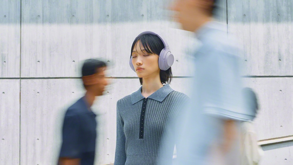 Slúchadlá Sony WH-1000XM4C fialová Žena pri chôdzi mestom má na sebe slúchadlá Sony WH-1000XM4C