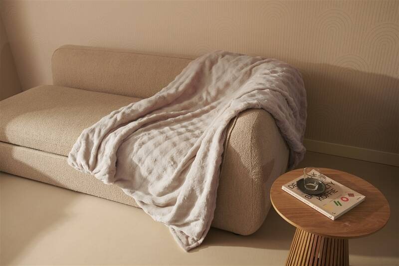 Vyhrievacia deka Duux DXOB12 Yentl Cuddle 200 x 200 cm sivá Nadrozmerná šedá deka Duux Yentl voľne prehodená cez textilnú pohovku vedľa dreveného stolíka s časopisom v jemne ladenom modernom obývacom priestore.