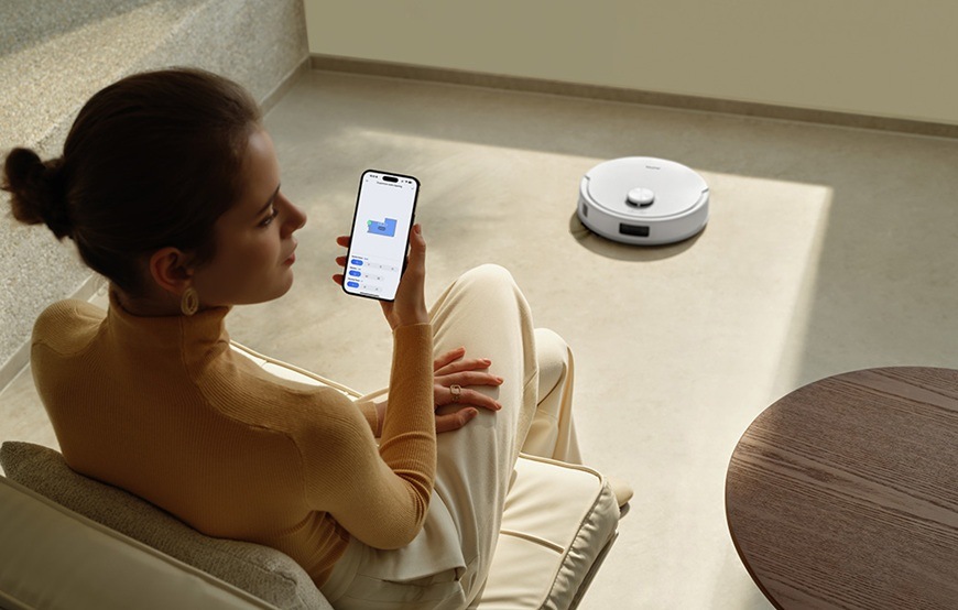Detail obrázku muža ovládajúci robotický vysávač pomocou mobilnej aplikácie.