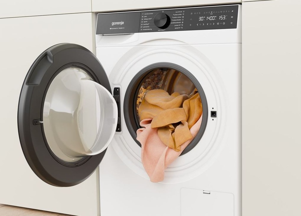 Práčka Gorenje G600 WG614A4P1 FastWashPro biela biela práčka gorenje fastwashpro zabudovaná v skrinovej stene. Visi z nej oranžovú bielizeň.