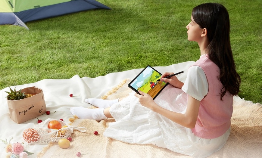 Žena sediaca na piknikovej deke v parku má rozkreslený obrázok na tablete UGEE UT2