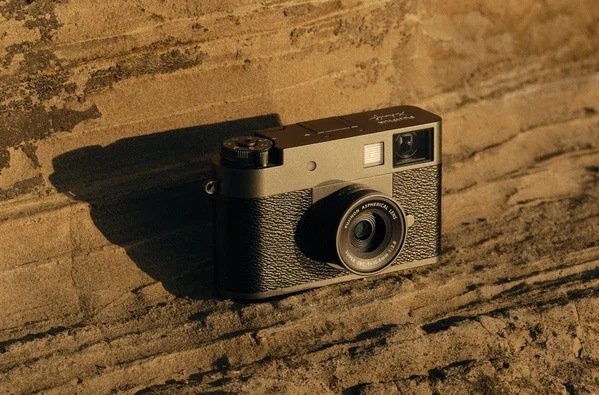 Digitálny fotoaparát Fujifilm X half strieborný Kompaktný fotoaparát Fujifilm X half opretý o kamenný múr, zvýrazňujúci retro vzhľad a pevnú konštrukciu