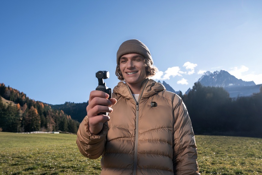 Outdoorová kamera DJI Osmo Pocket 4 Standard Combo čierna Muž stojaci na lúke drží kameru.