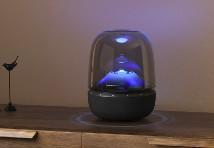 Reproduktor Harman Kardon Aura Studio 5 umiestnený na komode s modrým svetelným efektom