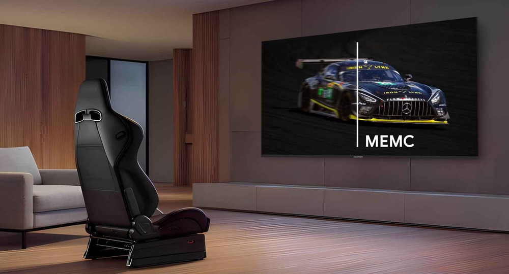 Elegantná, moderná miestnosť s kreslom v závodnom štýle s veľkou plochou obrazovkou zobrazujúcou závodné auto. Obrazovka ukazuje technológiu „MEMC“ v akcii.