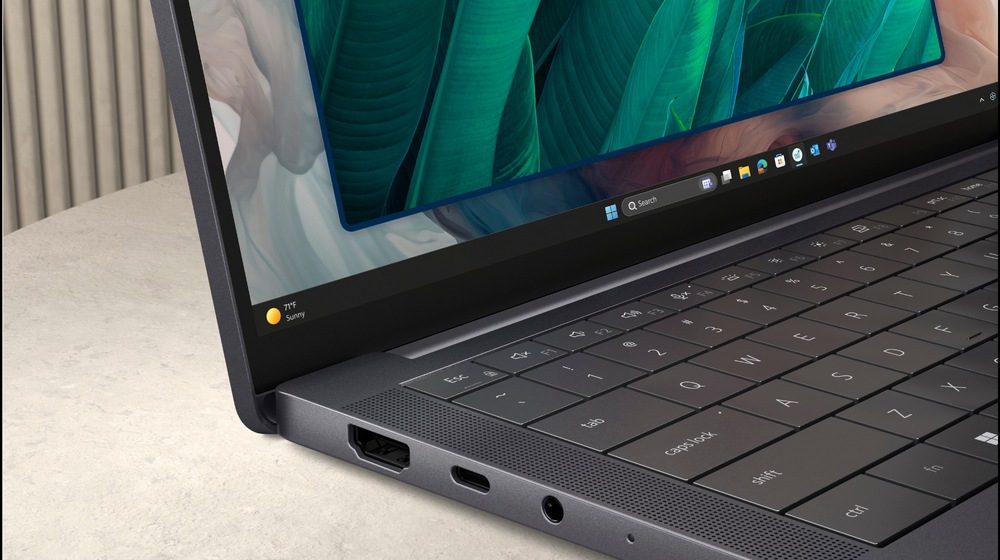 Elegantný notebook leží otvorený na svetlom povrchu a na jeho žiarivom displeji sa zobrazujú zelené listy. Strieborné telo je vybavené portami USB a HDMI.