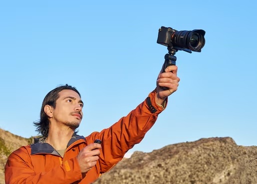 Muž v horách drží vo výške fotoaparát na gripe Sony GP-VPT3