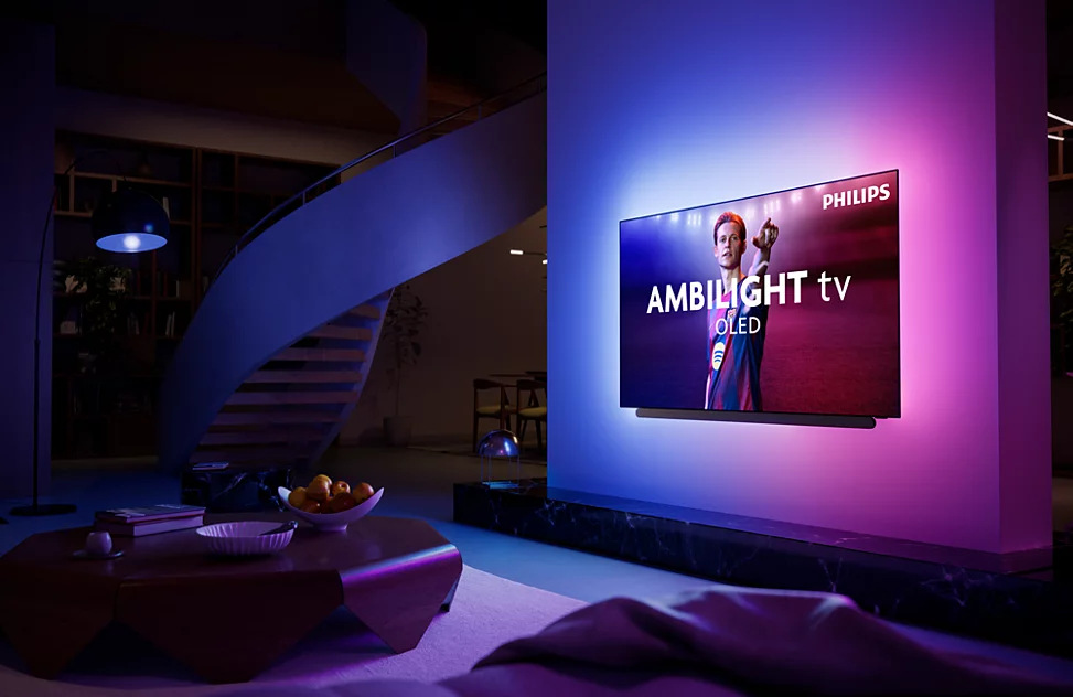 Televízia Philips OLED+ s Ambilight zavesená na stene obývacej izby, na obrazovke futbalový prenos.