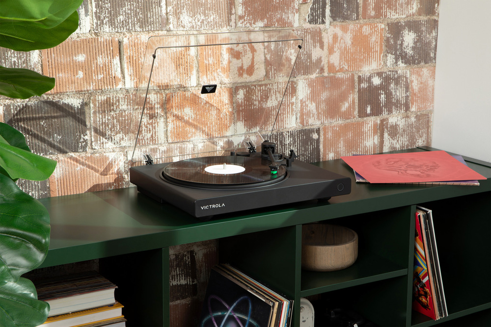 Gramofón Victrola VPT-1520 Wave umiestnený v modernom interiéri na skrinke, prehráva vinylovú dosku v obývacej izbe