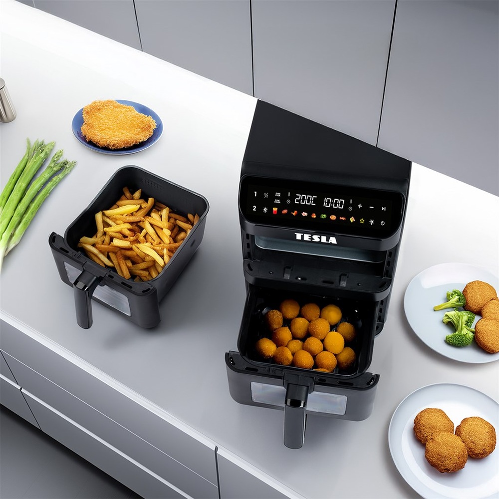 Teplovzdušná fritéza Tesla AirCook DualZone Q670 XXL stojí na kuchynskej linke, vedľa nej leží kôš fritézy s hranolkami a dva taniere s vyprážanými pokrmami.