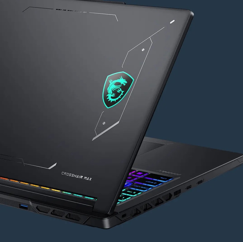 Notebook MSI Crosshair 16 Max HX E2WGXK-056CZ čierny Detail MSI Crosshair 16 Max HX E2W zozadu a zboku. Na tmavom veku svieti tyrkysový znak MSI s drakom, vidieť je aj farebne podsvietená klávesnica, bočné konektory a rozsiahle vetracie otvory