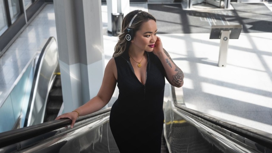 Žena idúca po eskalátore počúva hudbu zo slúchadiel Koss Porta Pro Wireless 2.0″ width=