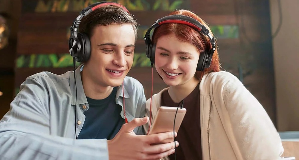 Slúchadlá OneOdio Slúchadlá Fusion A71M DJ s odnímateľným mikrofónom na ramienku čierna Muž a žena spoločne sledujú obsah na telefóne vďaka slúchadlám OneOdio Fusion A71M so zdieľaním zvuku