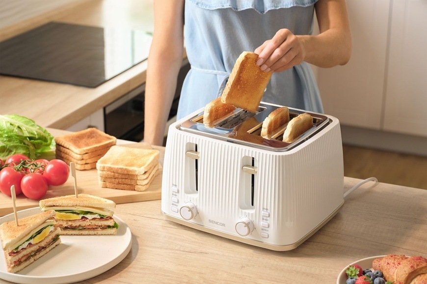 Hriankovač Sencor STS 7540WH biely Žena pripravuje raňajky a vyťahuje toast z hriankovača Sencor STS 7540WH v modernej svetlej kuchyni.