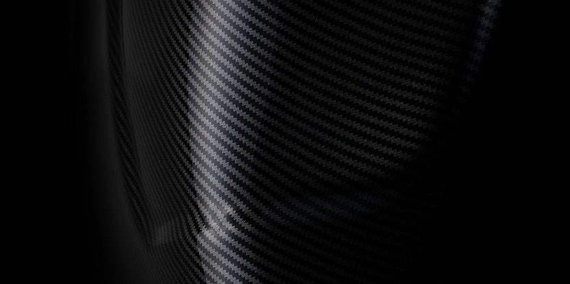 Detail zakriveného, ​​lesklého povrchu z uhlíkových vlákien, na ktorom je vidieť diagonálne vzory a jemné odrazy svetla. Obrázok vyžaruje elegantný, moderný dojem.