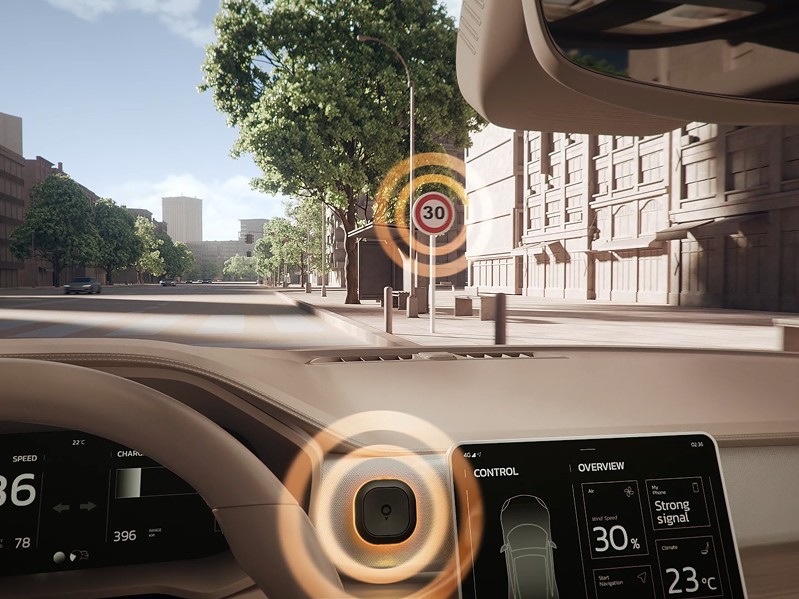 Pohľad z automobilu na mestskú ulicu s rýchlostným obmedzením 30 km/h. Cestovný asistent TomTom Tom na palubnej doske svieti oranžovým LED krúžkom a upozorňuje vodiča na prekročenie povolenej rýchlosti.
