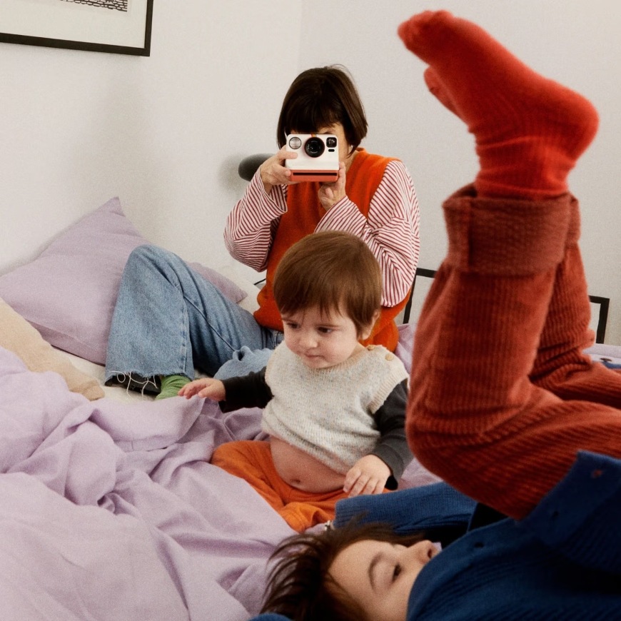 Žena fotografuje hrajúce sa deti pomocou instantného fotoaparátu Polaroid Now Gen 3″ width=