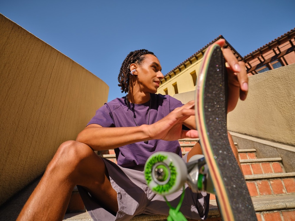 Slúchadlá Shokz OpenDots Air, Bluetooth fialová Muž sediaci so skateboardom a slúchadlami Shokz OpenDots Air v ušiach