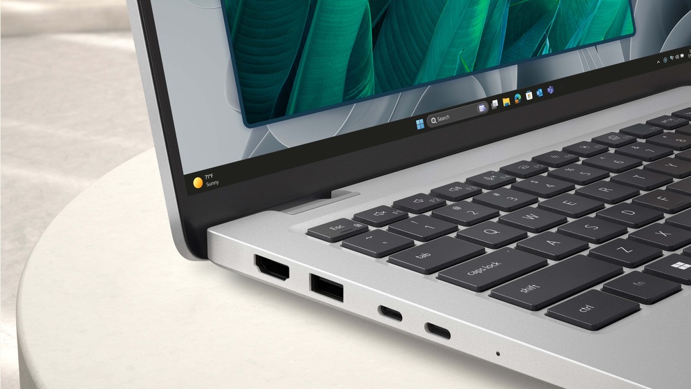 Notebook Dell Pro 14 PC14255 strieborný Elegantný notebook leží otvorený na svetlom povrchu a na jeho žiarivom displeji sa zobrazujú zelené listy. Strieborné telo je vybavené portami USB a HDMI.