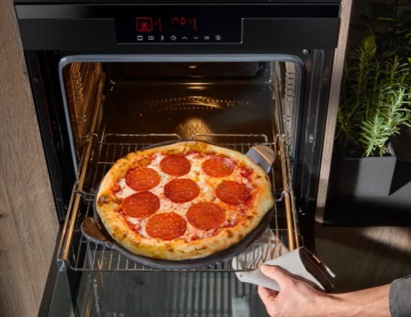 Rúra Amica ED3751BA V PIZZA STUDIO čierna/nerez Mužská ruka drží v utierke vysunutý rošt z rúry Amica. Na ňom leží prepečená pizza so salámou.