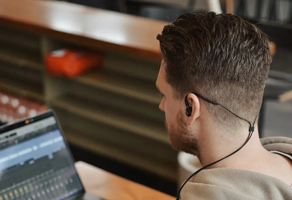 Muž upravujúci hudbu v notebooku má nasadené slúchadlá Beyerdynamic DT 70 IE