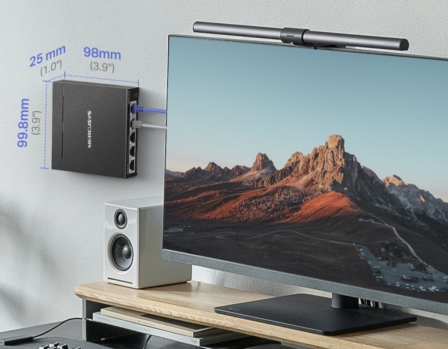 Switch Mercusys MS105GS-M2 (MS105GS-M2) čierny Switch Mercusys pripevnený na stene vedľa monitora. Obrázok uvádza kompaktné rozmery 99,8 × 98 × 25 mm.