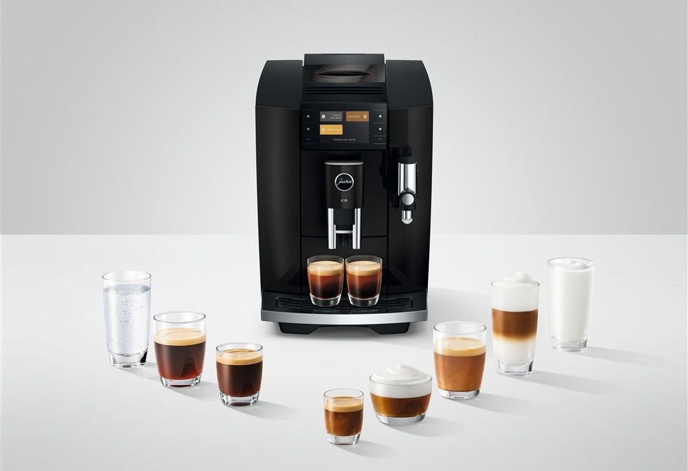 Automatický kávovar Jura E8 Piano Black pripravuje dve šálky kávy zároveň, okolo kávovaru je rozostavaných osem pohárov s rôznymi druhmi kávy