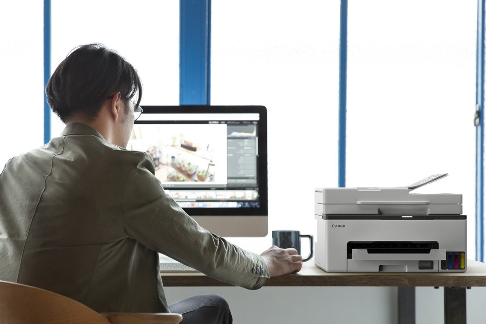 Muž pracujúci pri monitore s tlačiarňou Canon MAXIFY GX2040 na stole v kancelárii.