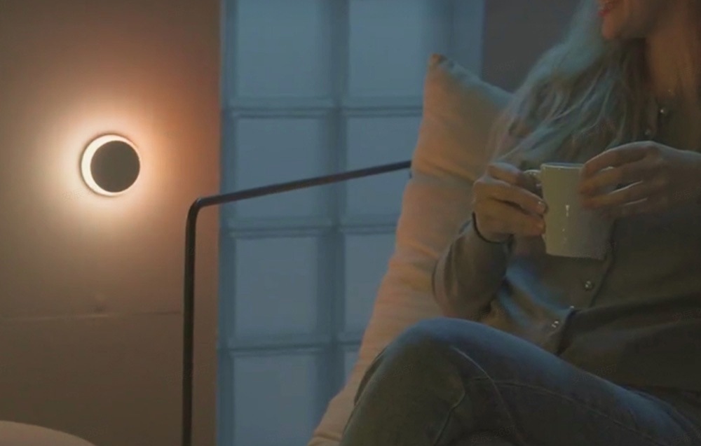 Nočné svetlo Yeelight Vega RGB NightLight s pohybovým senzorom biele Žena sedí v obývacej izbe so šálkou čaju av zásuvke má svetlo Yeelight Vega RGB NightLight