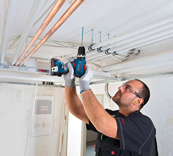 Vŕtací skrutkovač Bosch Professional GSB 18V-65 (s baterií) Remeselník vŕtajúci nad hlavou pomocou Bosch Professional GSB 18V-65 pri montáži inštalácií