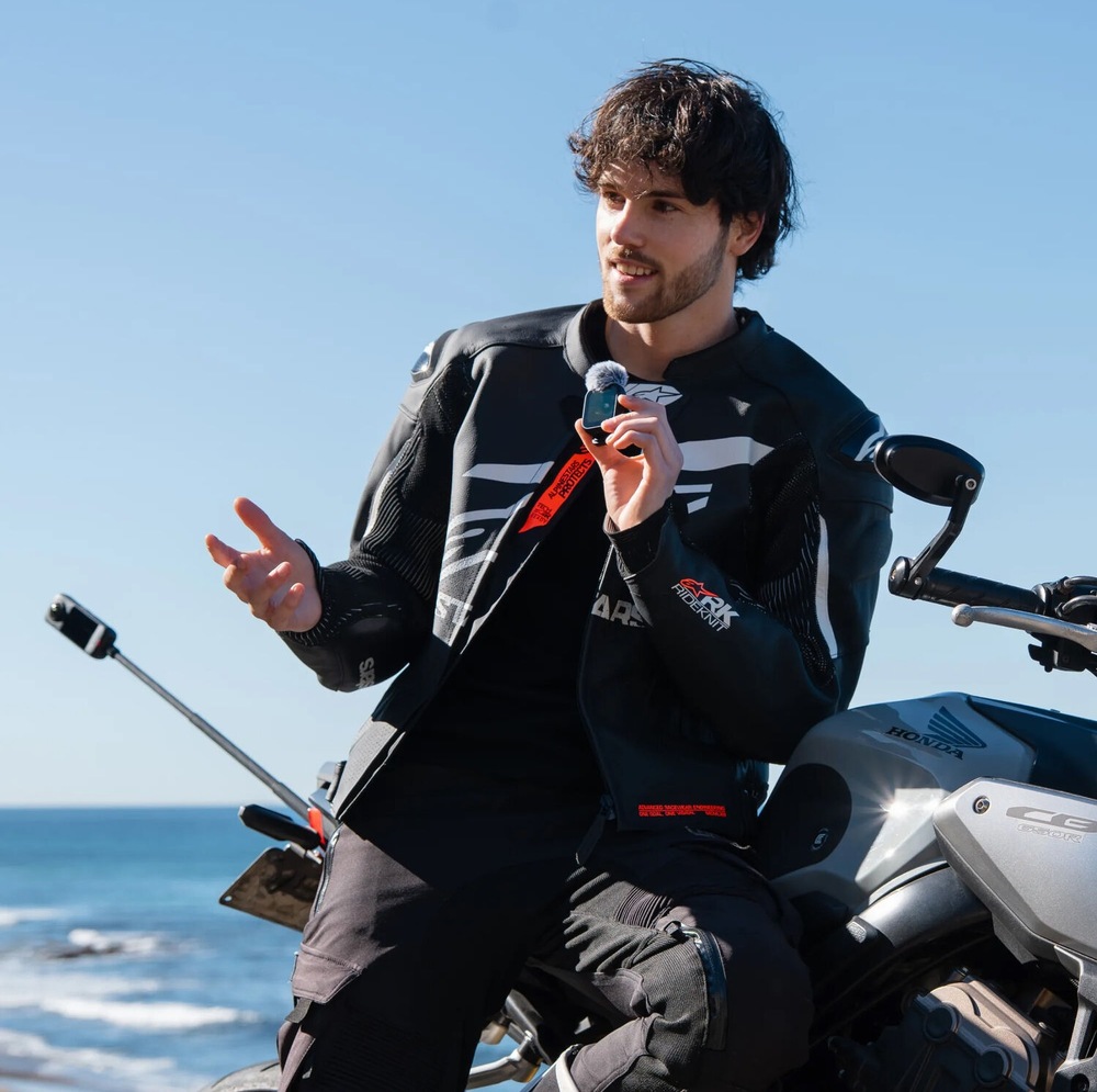 Motorkár sedí na motocykli a hovorí do mikrofónu na diaľkovom ovládači Insta360 GPS/MIC