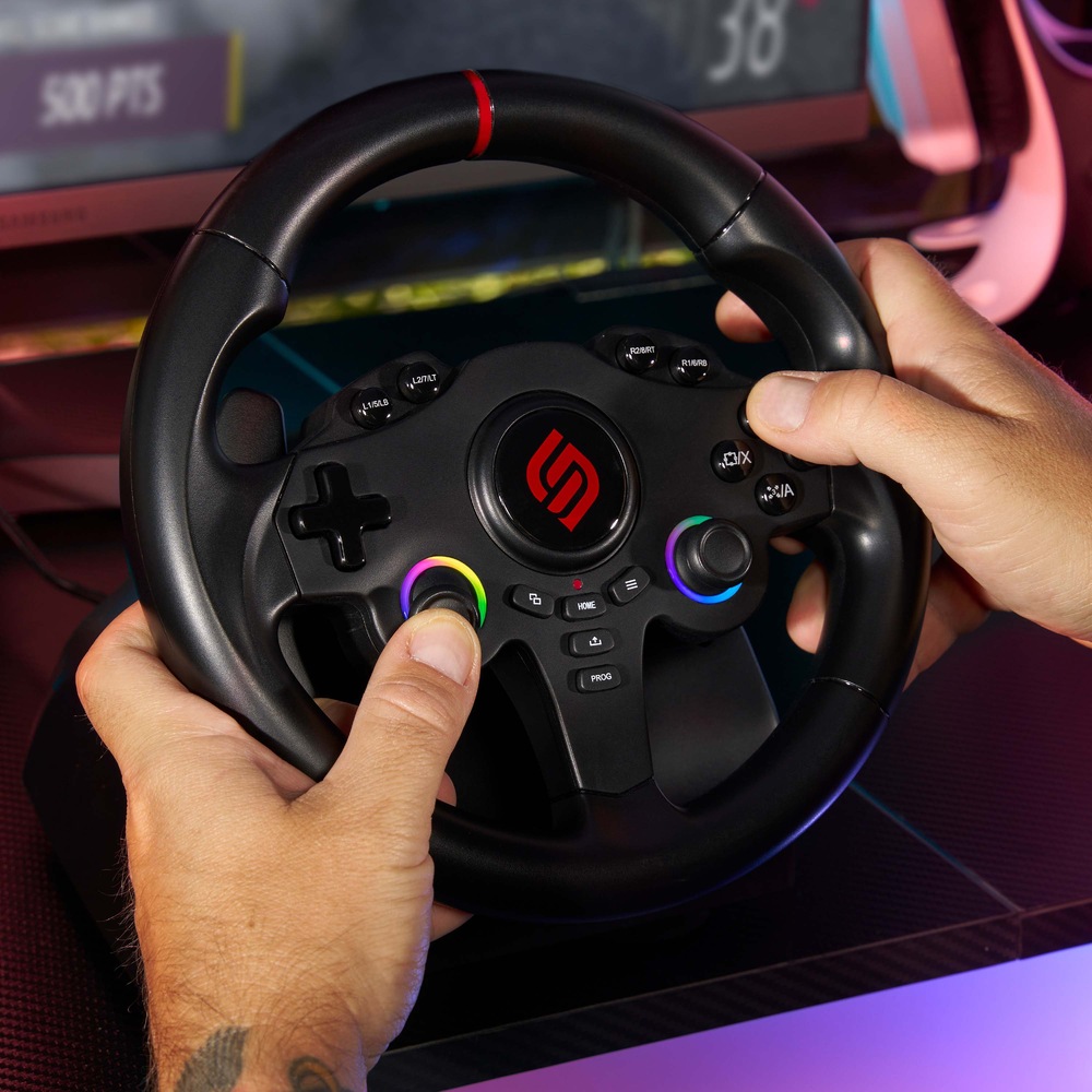Volant SUPERDRIVE 220 RS-5 čierny Ruky zvierajú čierny herný volant s farebnými tlačidlami pred monitorom zobrazujúcim virtuálnu závodnú hru. Energický a sústredený tón.