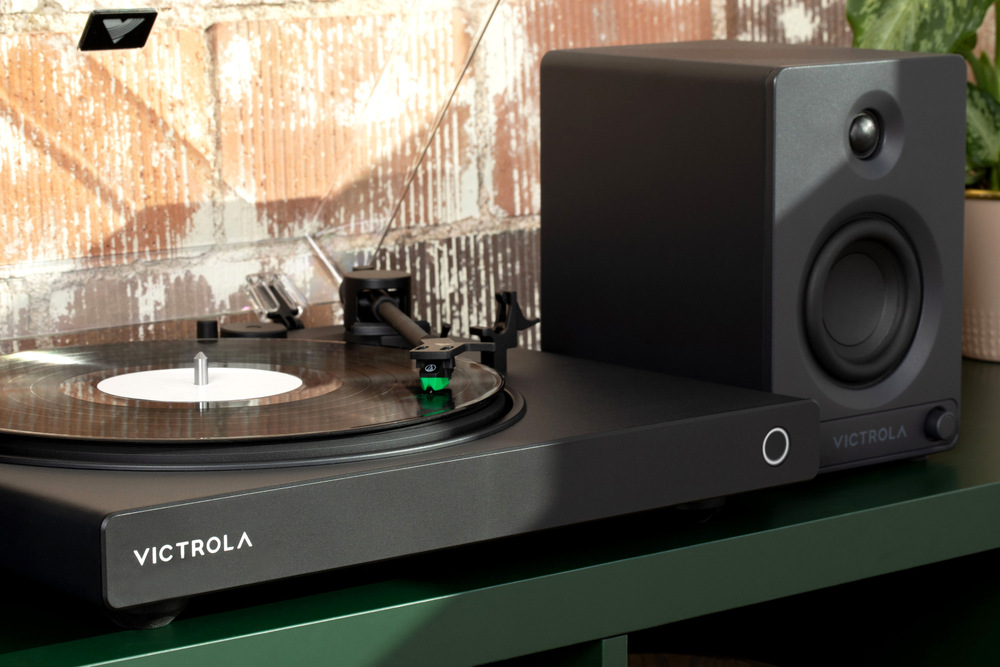 Detail gramofónu Victrola VPT-1520 Wave prehrávajúci vinyl, pripojený k externému reproduktoru na polici v domácom prostredí