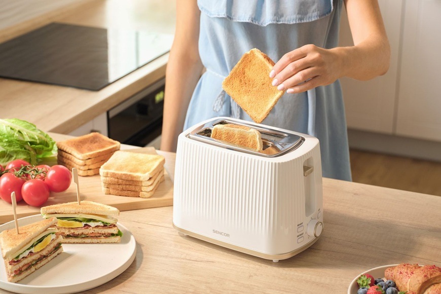 Hriankovač Sencor STS 7510WH biely Žena dáva toast do hriankovača Sencor STS 7510WH. Na linke sú hrianky, toasty, paradajky a šalát.