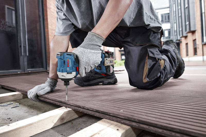 Doťahovák rázový Bosch Professional GDR 18V-215 (bez baterie) Muž kľačí na zemi na stavbe a vŕta s Rázovým uťahovákom Bosch Professional GDR 18V-215