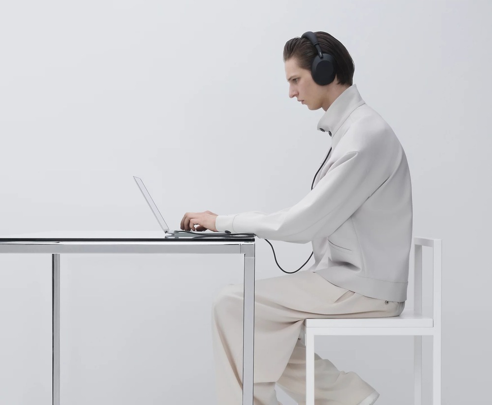 Slúchadlá Sony WH-1000XM6, Noise Cancelling - Bezplatné predĺženie záruky po registrácii ružová Muž sediaci pri stole pracuje na notebooku, ku ktorému má káblom pripojené slúchadlá Sony WH-1000XM6