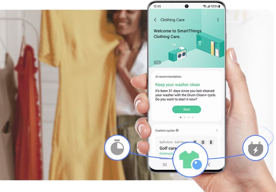 Ruka drží telefón, na ňom je aplikácia Samsung SmartThings a upozornenie, že sa 31 dní nepúšťal program na čistenie práčky. V pozadí je žena, ktorá sa túli k žltým šatám