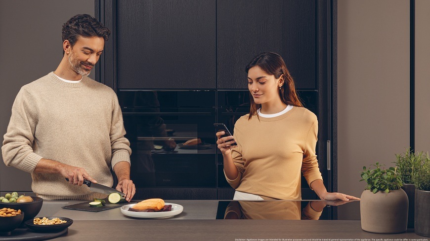 Rúra Haier H6 ID2P3B4VYTB čierna/sklo rúra Haier H6 ID2P3B4VYTB dvaja ľudia sú pri kuchynskej linke, muž krája cuketu, žena pomocou mobilu ovláda rúru, ktorú majú za sebou