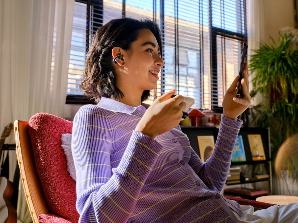 Slúchadlá Shokz OpenDots Air, Bluetooth fialová Žena so slúchadlami Shokz pri videohovore a pití kávy