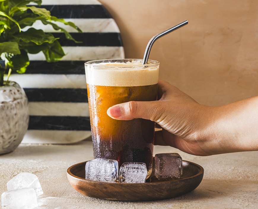 Žena drží v ruke osviežujúci Cold Brew. Okolo kávy sú kocky ľadu.