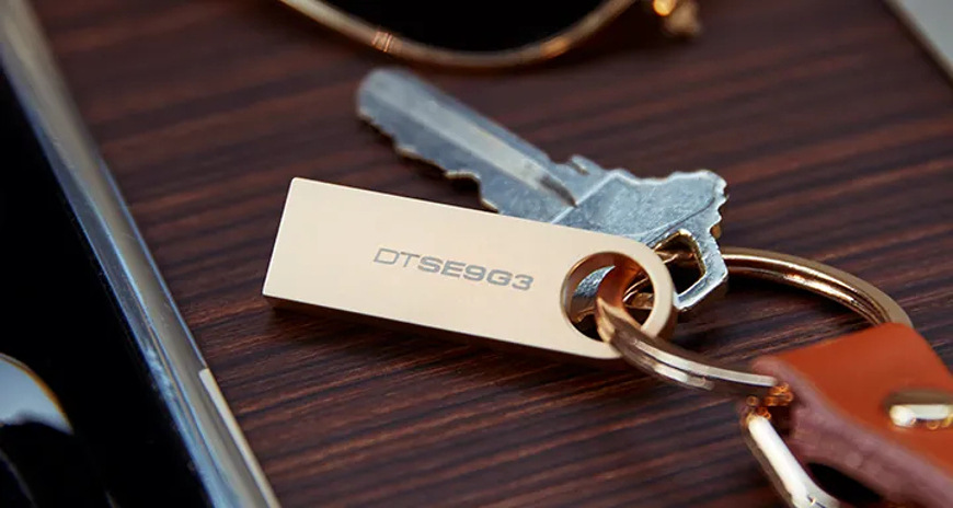 USB flashdisk Kingston DataTraveler SE9 G3 128GB zlatý Zlatý variant USB flashdisku Kingston DataTraveler SE9 G3 pripevnený ku kľúčom pomocou integrovaného očka, demonštrujúce ľahké prenášanie a odolné kovové prevedenie