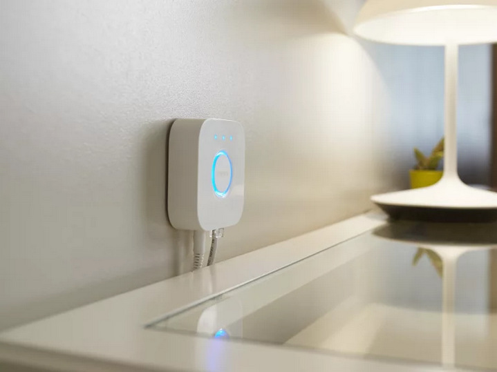Inteligentná žiarovka Philips Hue 4.2W, GU10, White and Color Ambiance, 3 ks + Ovládač Philips Hue Bridge 2.0 Ovládač Philips Hue Bridge 2.0 umiestnený na stene nad stolíkom.