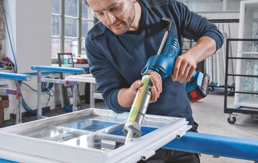 Lis Bosch Professional GCG 18V-310 (bez baterie) Muž v dielni používa vytláčaciu pištoľ Bosch na silikón a utesňuje sklenenú výplň na okne.