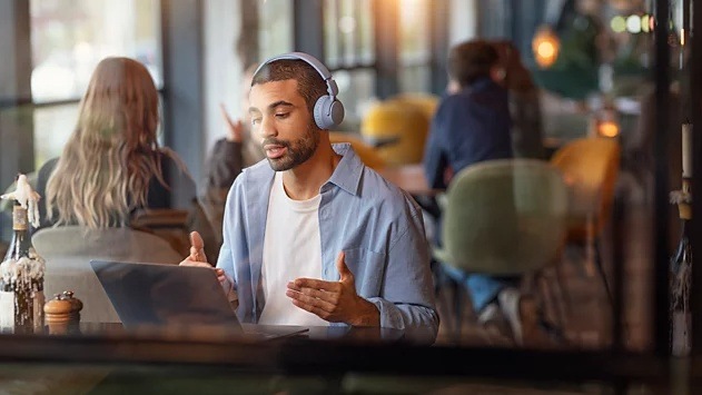 Muž v kaviarni telefonuje pomocou notebooku a slúchadiel Philips TAH4500