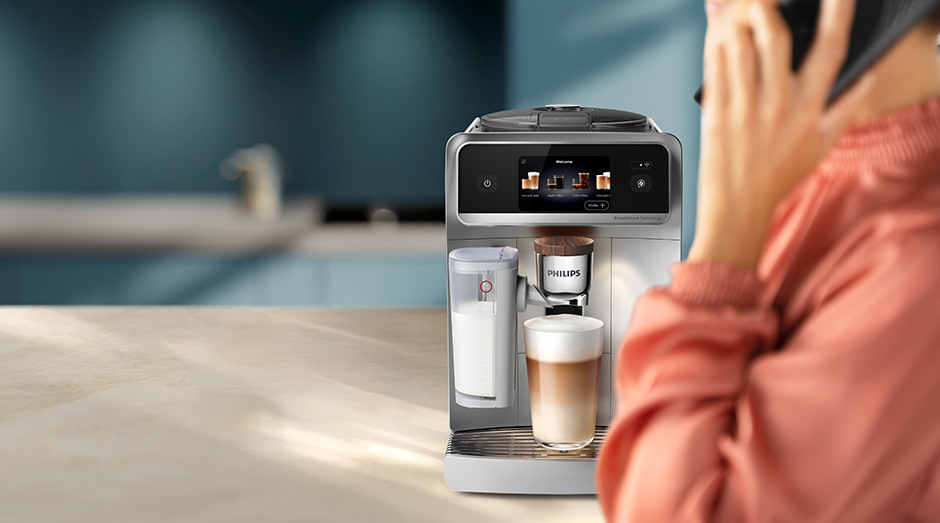 Automatický kávovar Philips EP8757/20 8000 Series pripravujúce latte a žena počas toho telefonuje