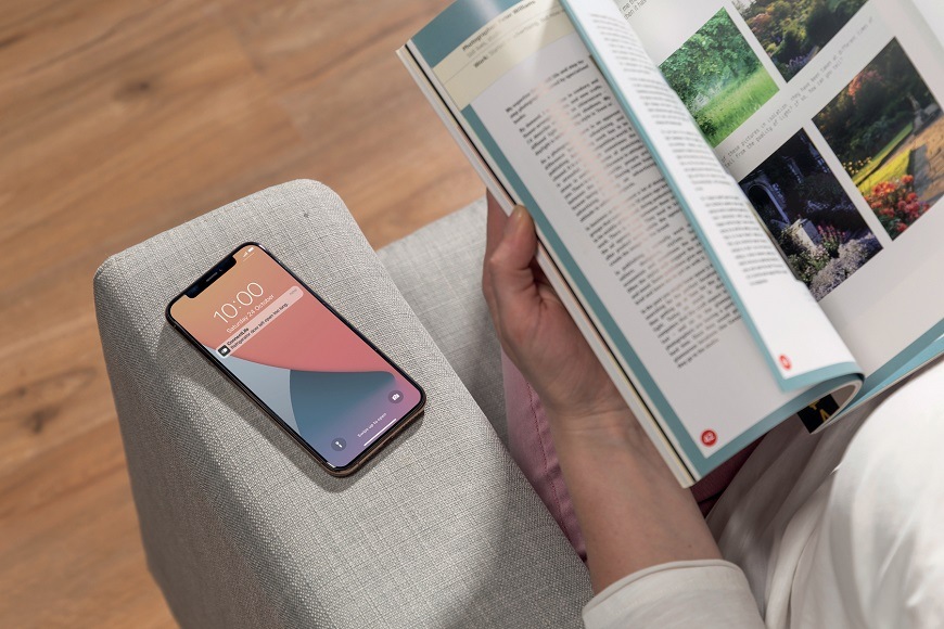 človek číta knihu s obrazkami a vedľa neho je na kresle mobilný telefón s notifikáciou od ConnectLife.